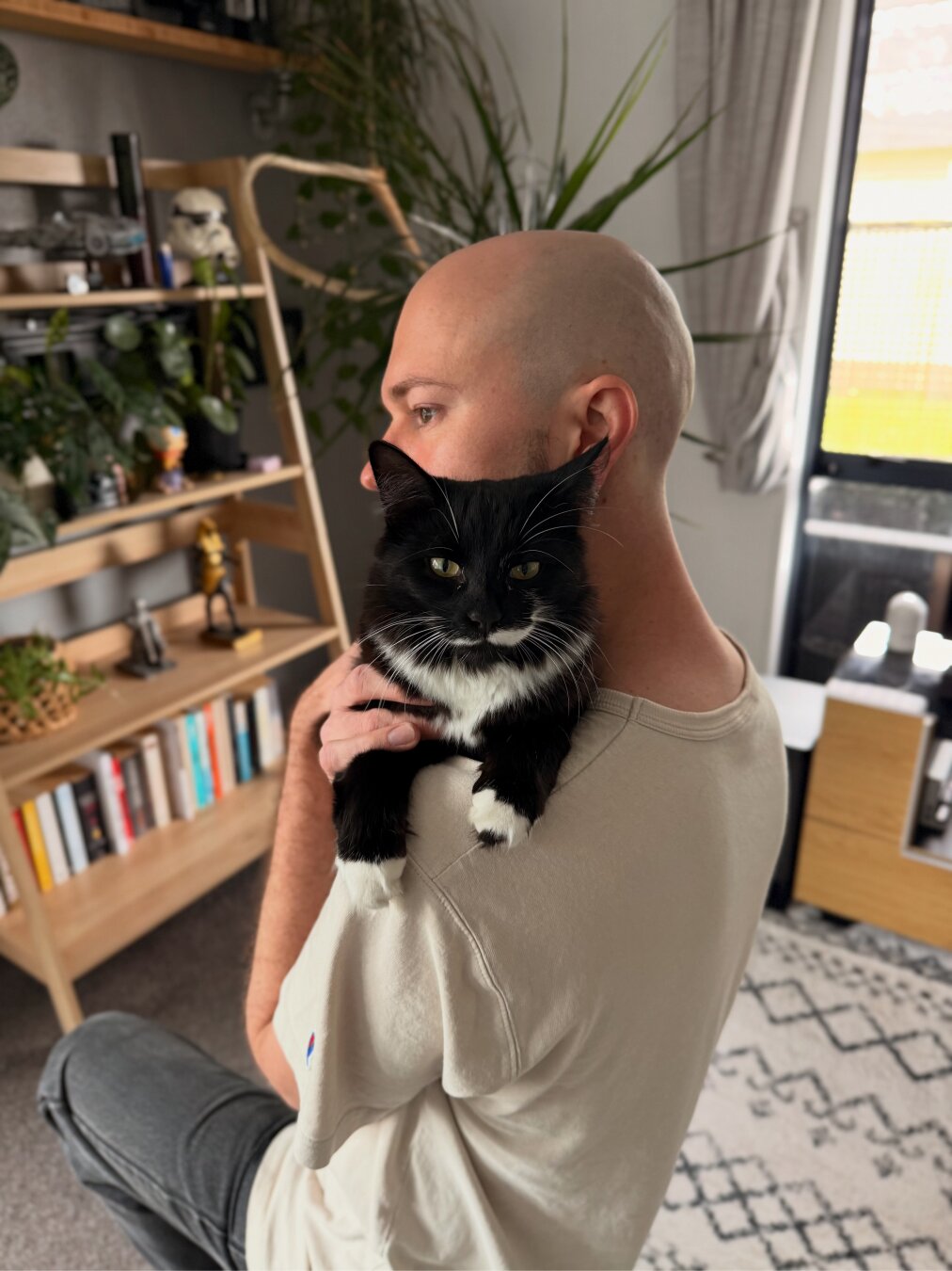 A bald dude snuggling a fluffy black cat.