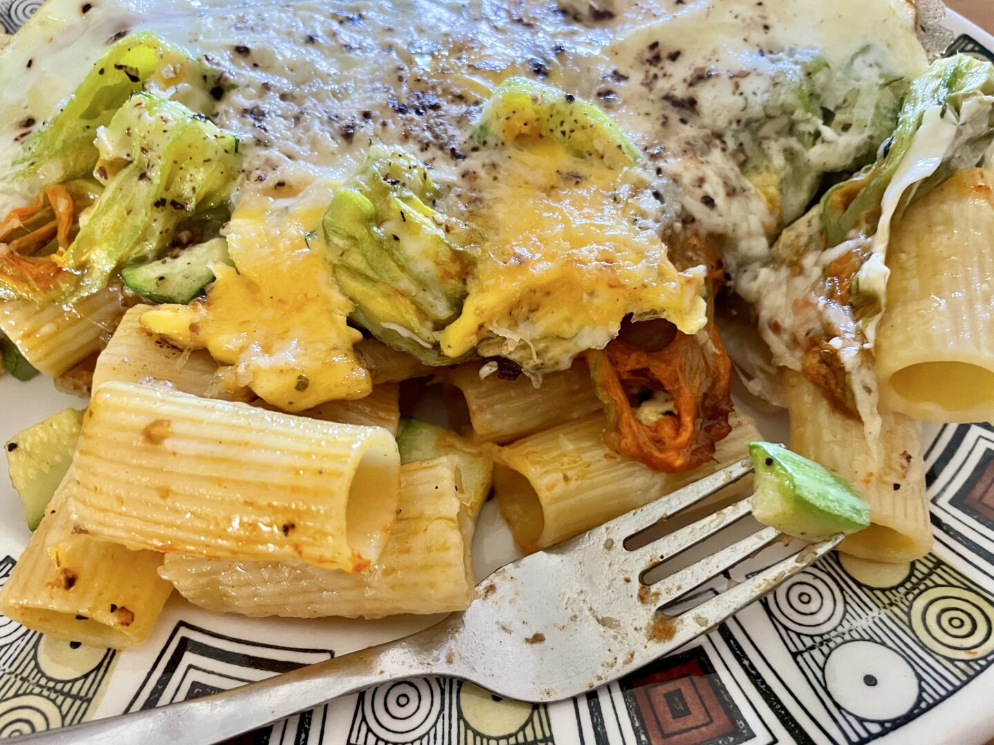 A fork and a Kathy Winkel plate filled with rigatoni and baked zucchini flowers in egg with melted cheese.