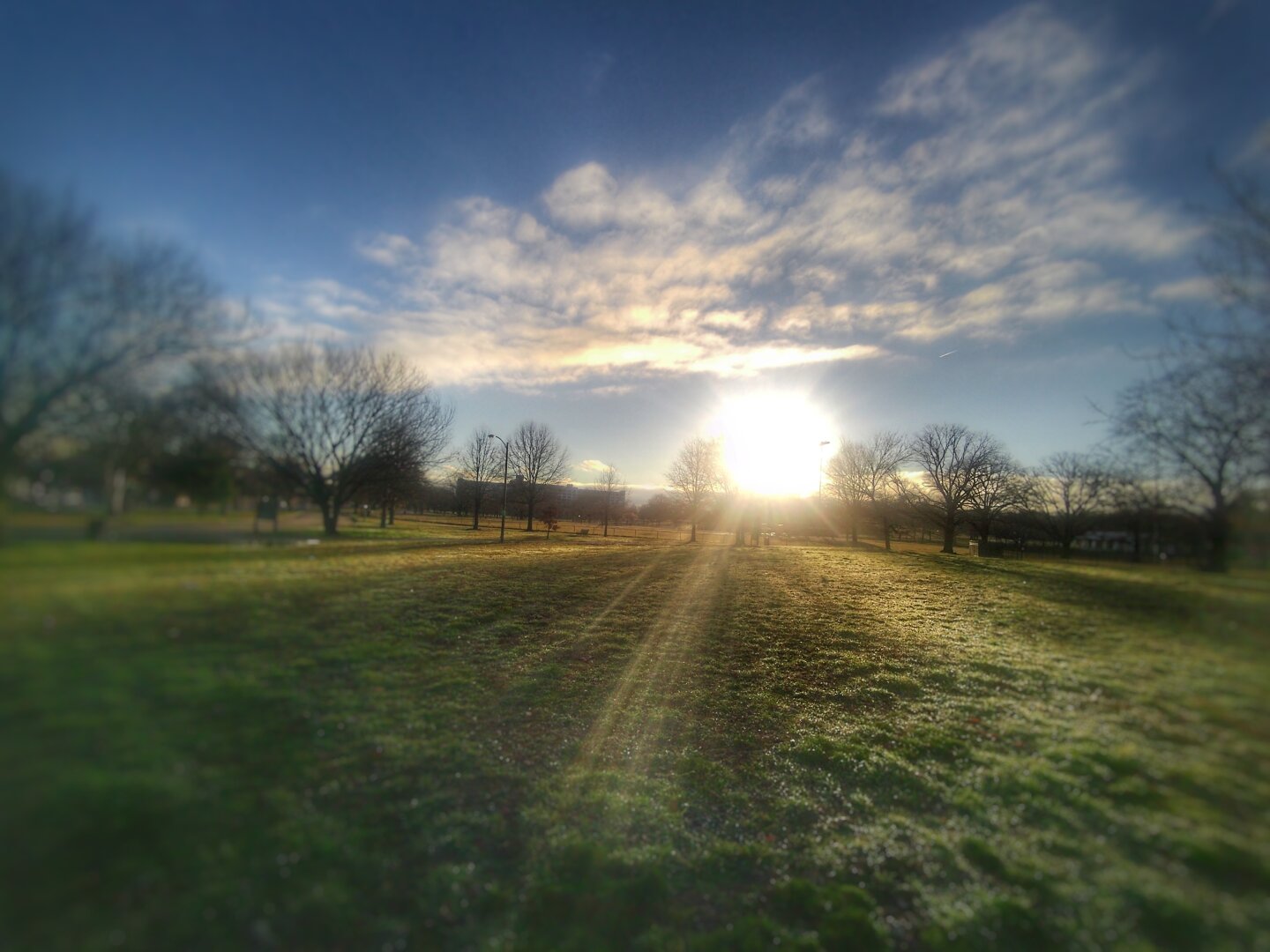 The sun, still fully visible, but at the horizon, shines on an open field at Carroll Park in Baltimore.
