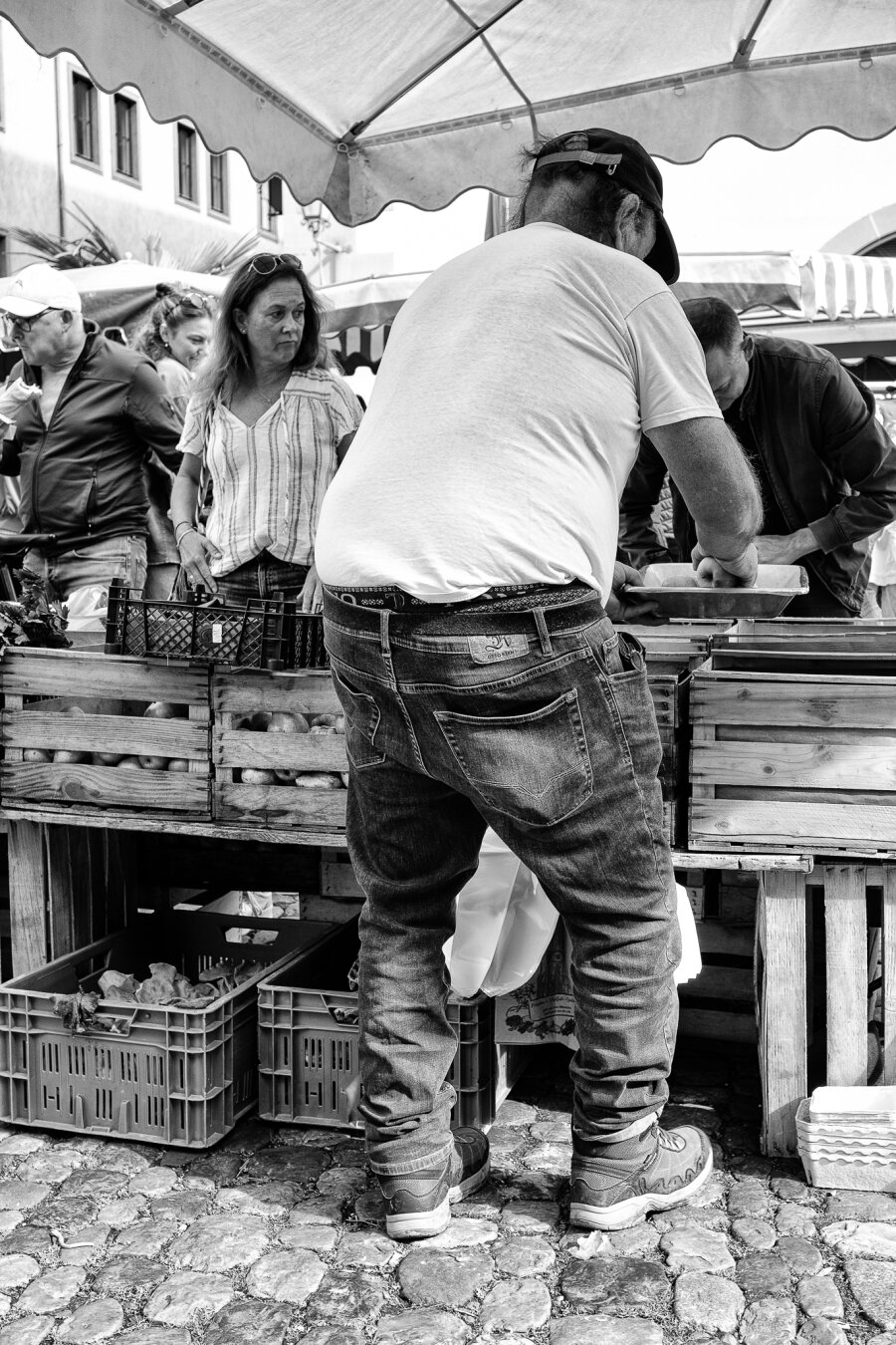 Market vendor seen from behind, selling apples.