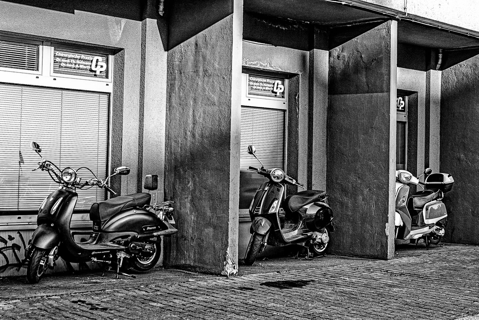 3 scooters are parked in a wall niche with their headlights to the left.