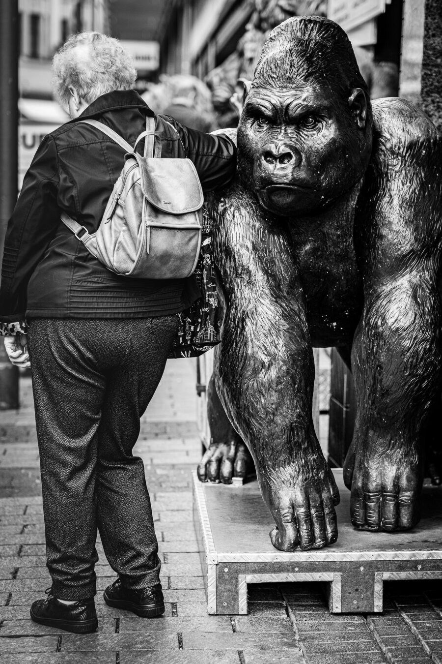 An elderly woman leans against a gorilla statue.