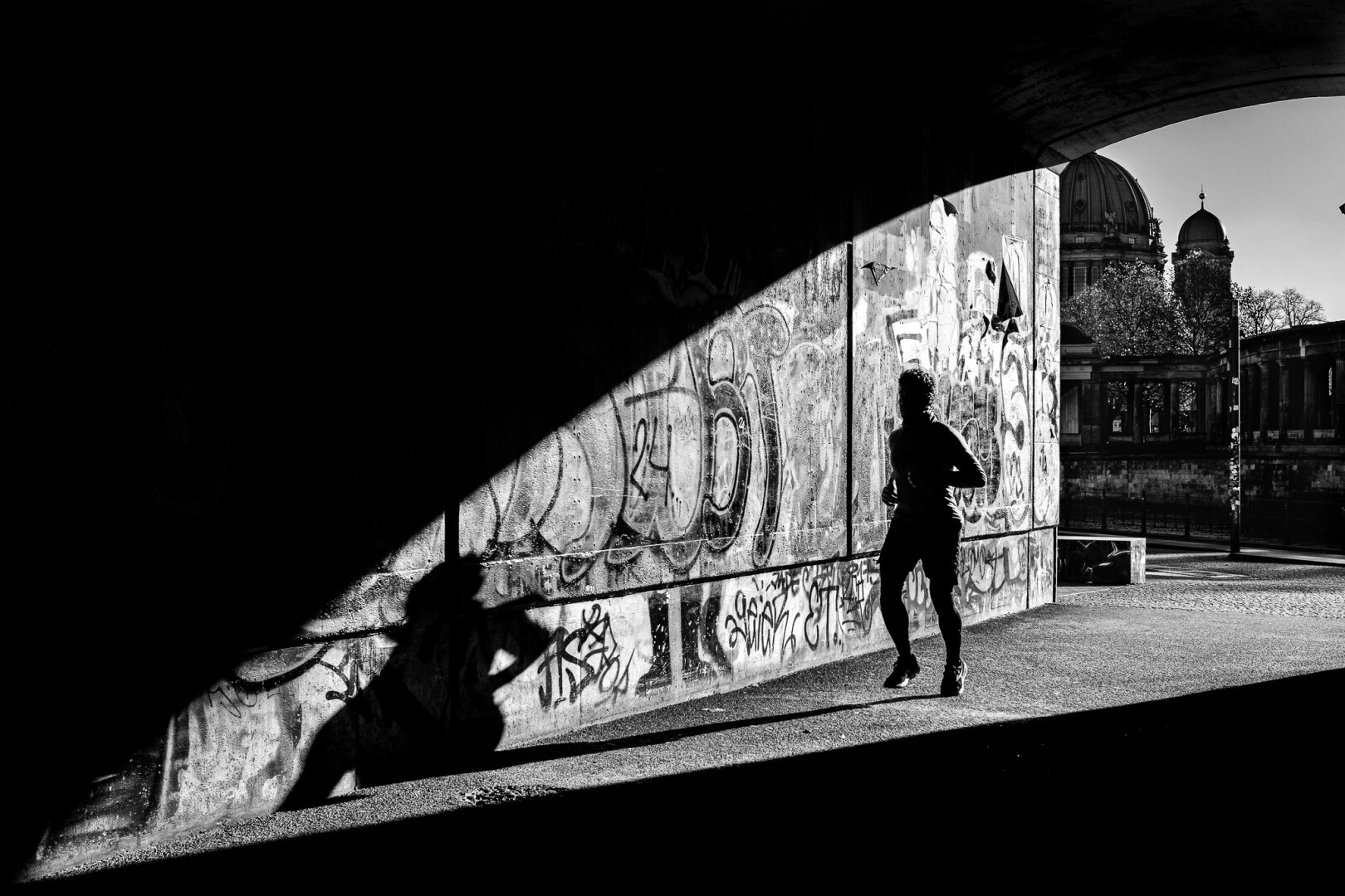 A backlit photograph of people walking, jogging, or cycling into a dark tunnel.