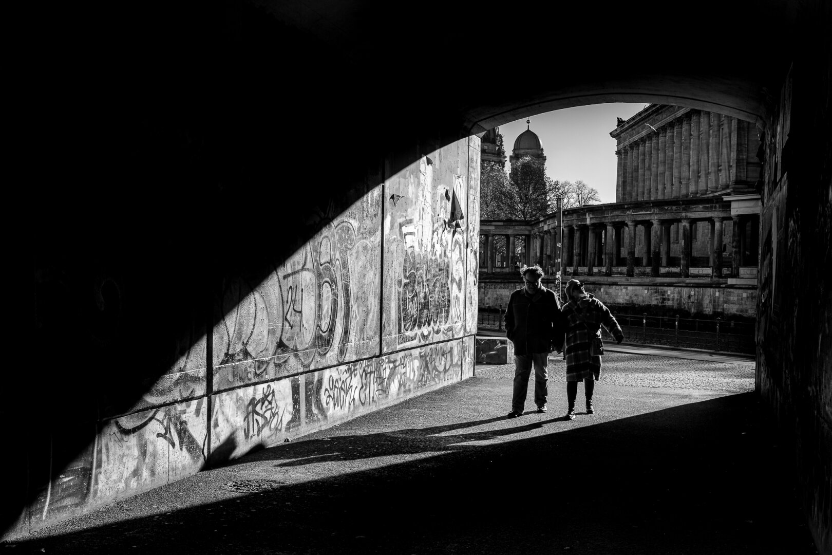 A backlit photograph of people walking, jogging, or cycling into a dark tunnel.