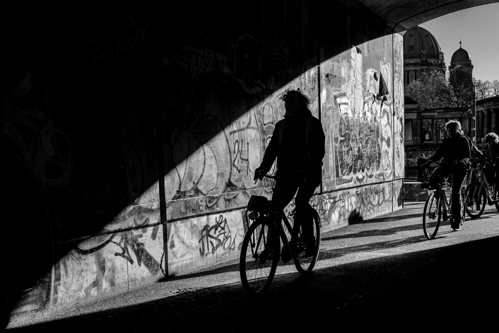A backlit photograph of people walking, jogging, or cycling into a dark tunnel.