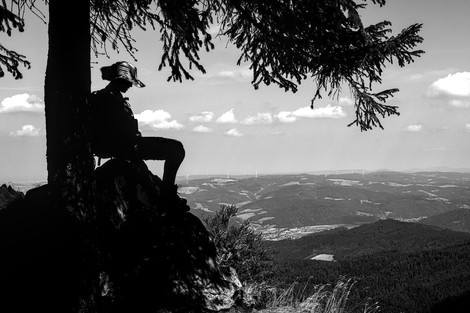 A woman takes a break from her trek. A black-and-white photograph with strong contrasts; only the woman’s silhouette is visible.