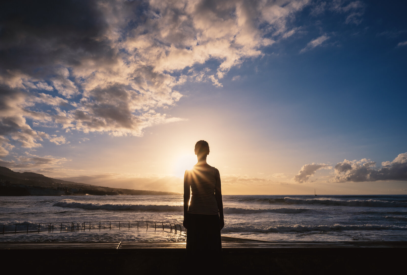 A female figure is standing in the middle of the frame looking into beautiful sunset over the sea