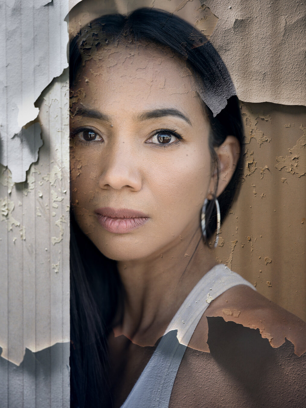 Fine art portrait of a woman partially obscured by a wall, combined with peeling paint textures. The textured layers extend across the face, hair and clothing, creating the impression that the portrait is gradually becoming part of the wall.