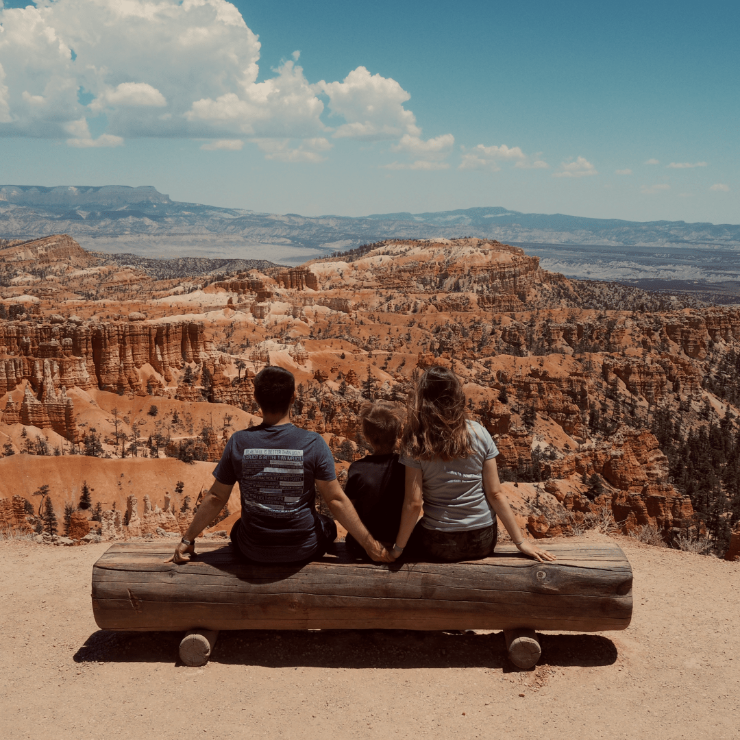 Three people sitting on a wooden log looking away from the camera at Bryce Canyon in the distance