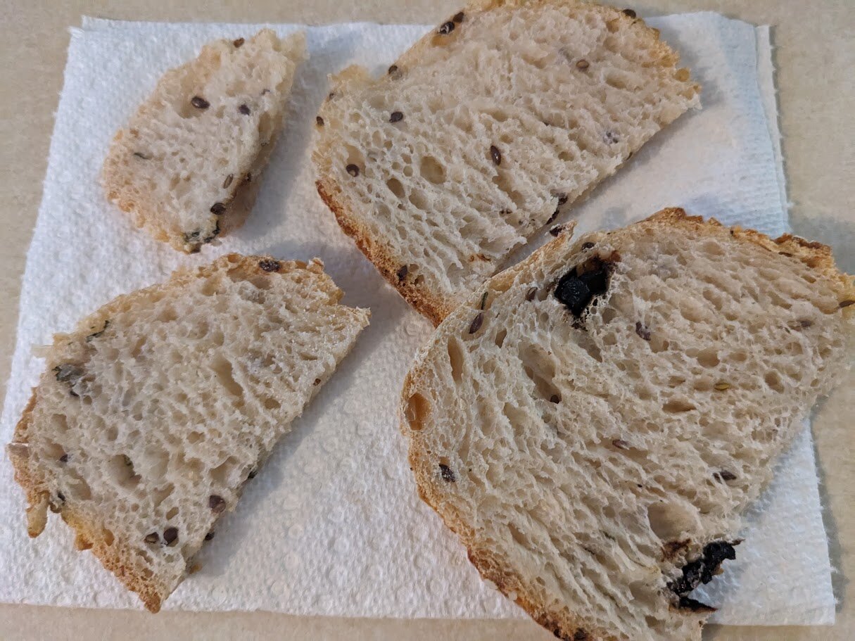 Four slices of the bread laid on a paper towel show more black garlic pieces and display the crumb structure.