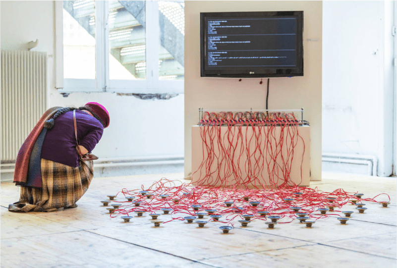 installation oh my() de noriyuki suzuki, un écran, en dessous un bloc ordinateur et des dizaines d'enceintes, une spectatrice est accroupie devant