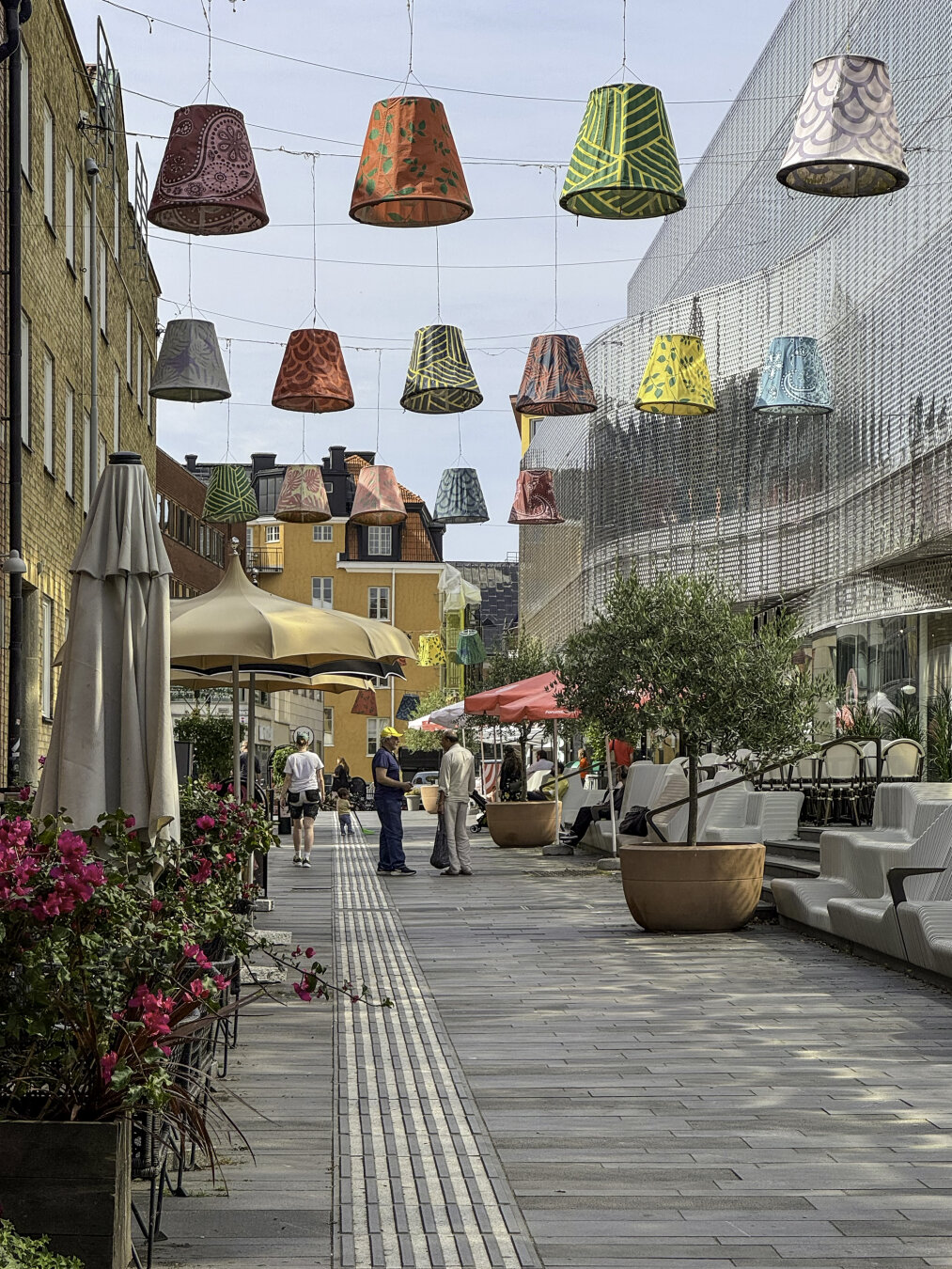 View down a pedestrian shopping street with decorative lampshades-as-art hanging above the street.