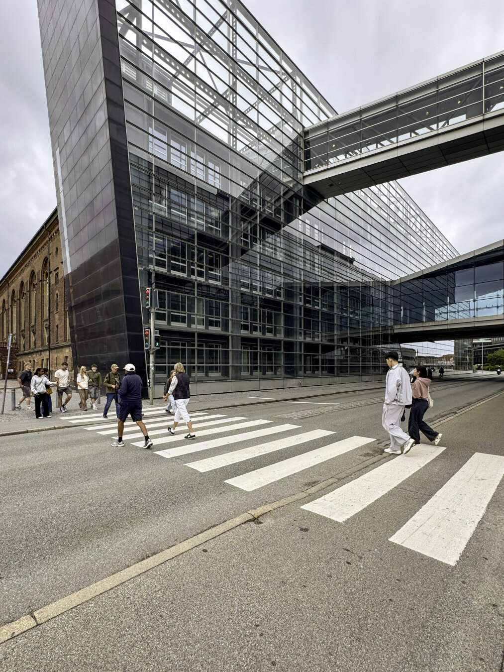 Pedestrians on a crosswalk next to a modern building that slightly cantilevers over the crosswalk.