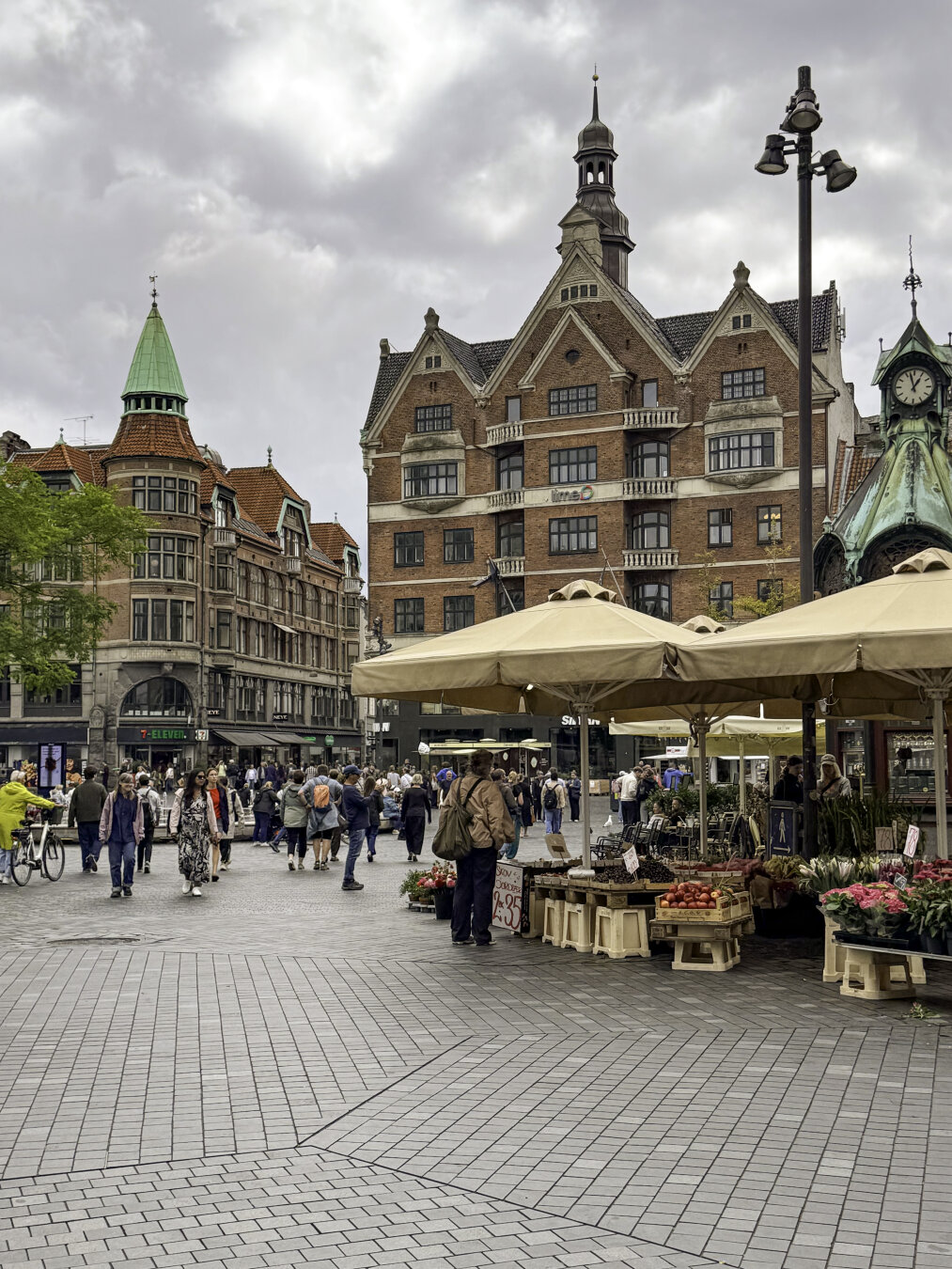 A pedestrian plaza is surrounded by beautiful historic buildings with pointy towers. Multiple vendors in tents line the walkway.