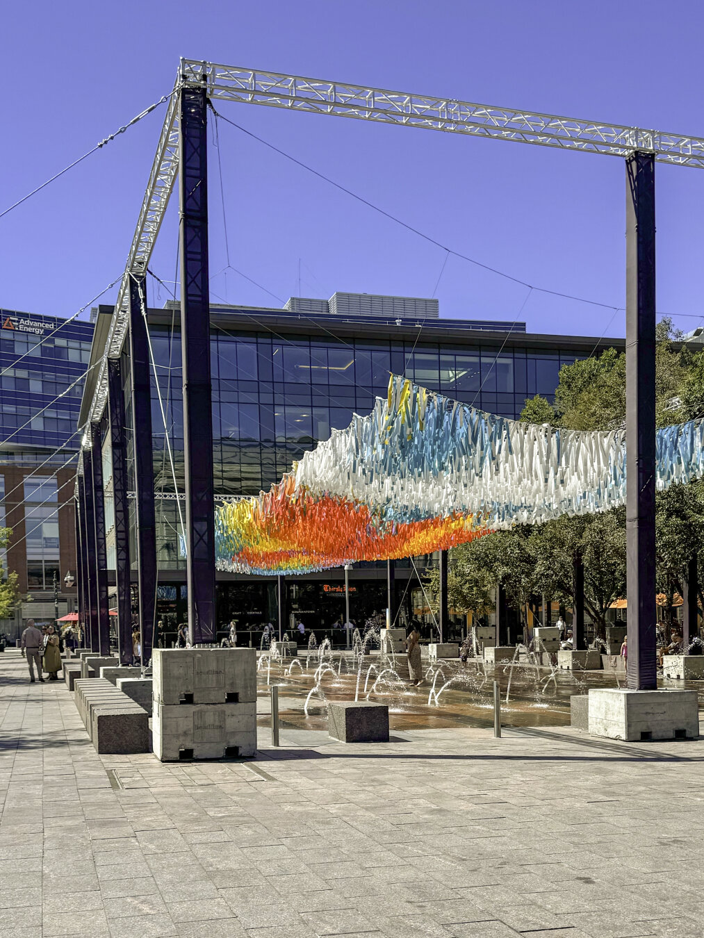 Steel framework above a large fountain holds thousands of colored ribbons floating in the breeze above the fountain.