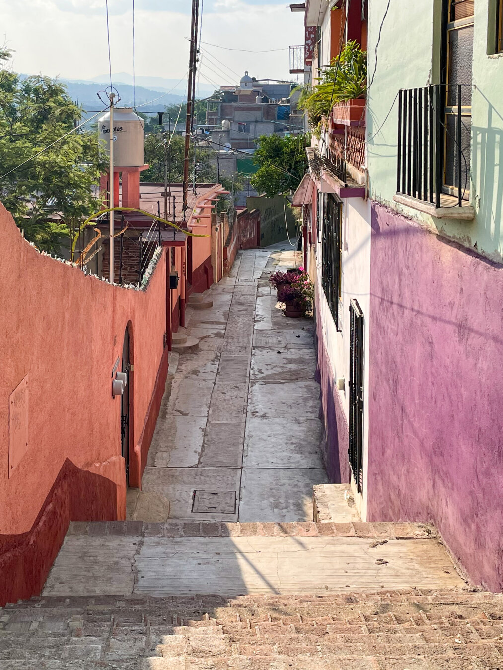 Narrow alleyway on a hillside with a series of stairs in between colorful painted walls and building facades.