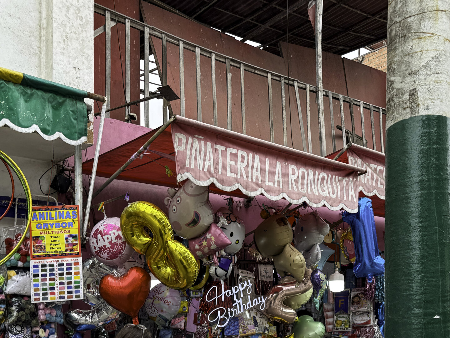 Sign above a storefront reading "piñatería" with numerous balloon and other party favors visible below.