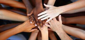 Foto che ritrae molte mani, con diversi coliri della pelle, che si unicono una sopra l'altra a formare una sorta di fraternità.