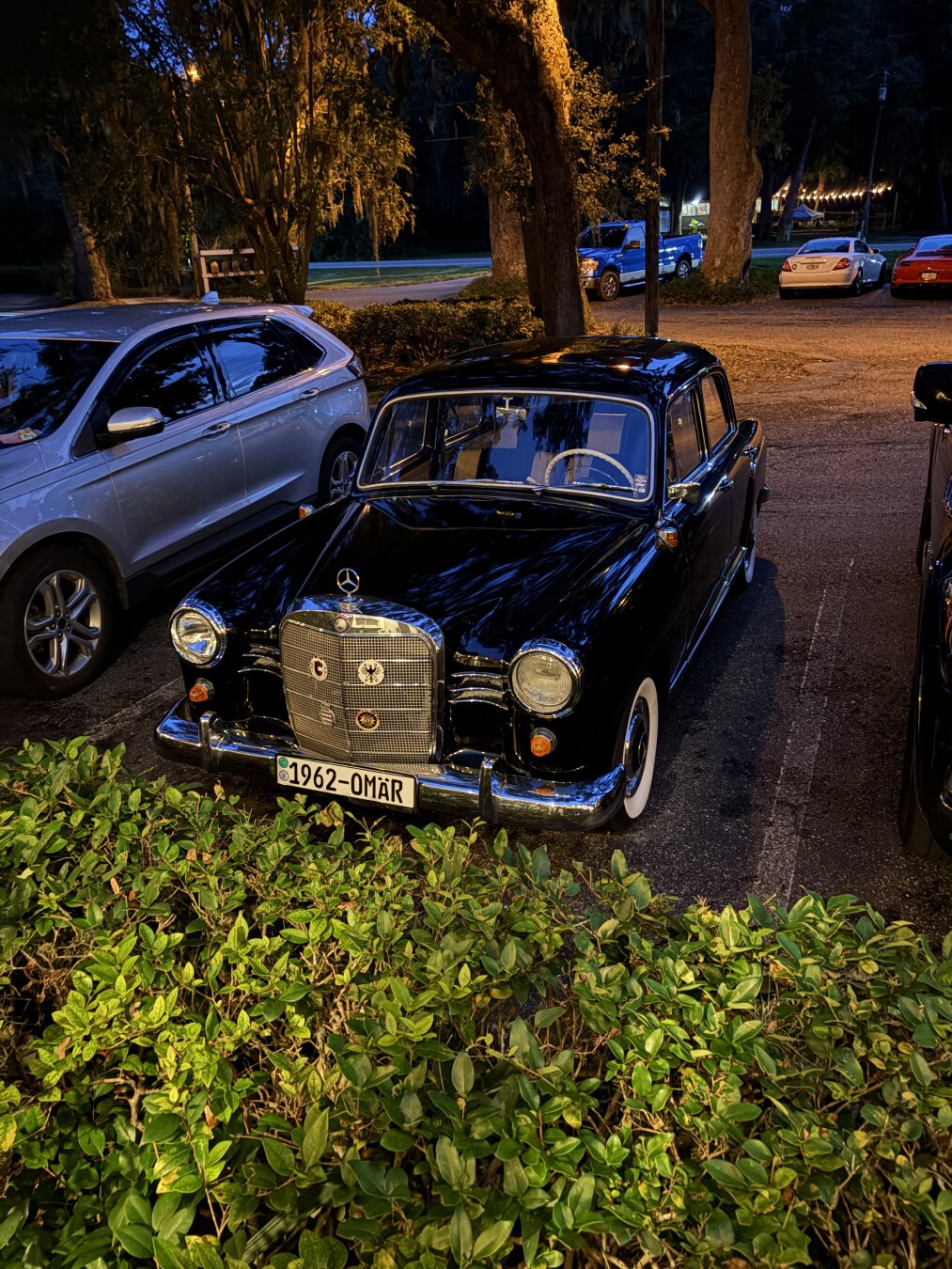 Picture of a 1962 Mercedes Benz sedan at night outside a restaurant.