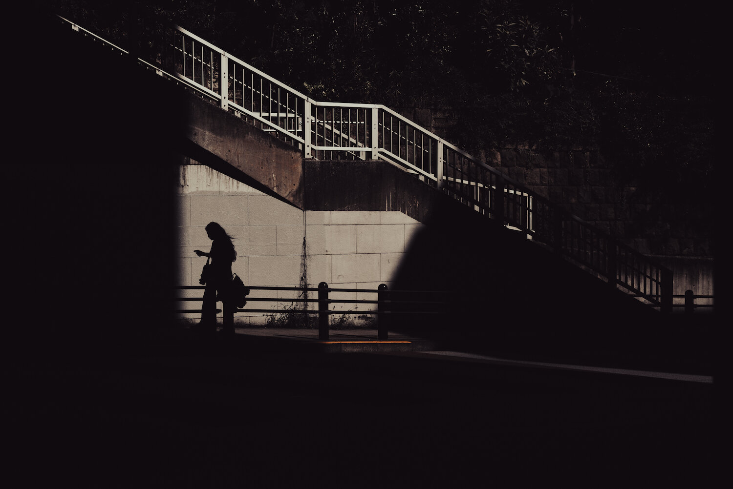 A misty morning silhouette of high-rise buildings in Nogizaka, Minato Ward. Towering structures and a cluster of traffic lights stand against a light, atmospheric sky, casting dark, geometric forms over the quiet street below. The scene is rendered in deep, textural black and white, capturing a fleeting urban moment.