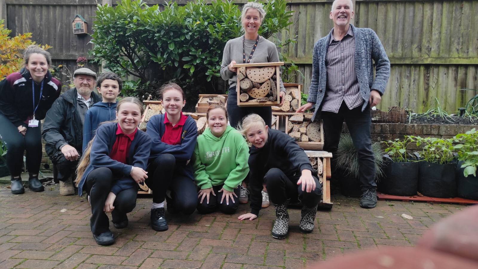 Group of school children and a couple of adults by wall smiling in group photo