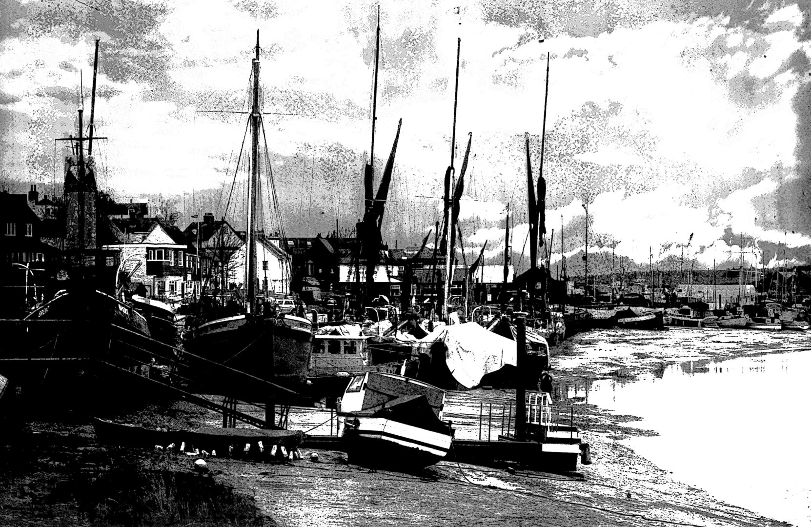 This evocative black-and-white image captures a row of historic Thames sailing barges moored at low tide along Hythe Quay in Maldon, Essex UK, a renowned maritime heritage site. These iconic vessels are distinguished by their tall masts, flat-bottomed hulls, and rich history as working cargo boats along the Thames Estuary.