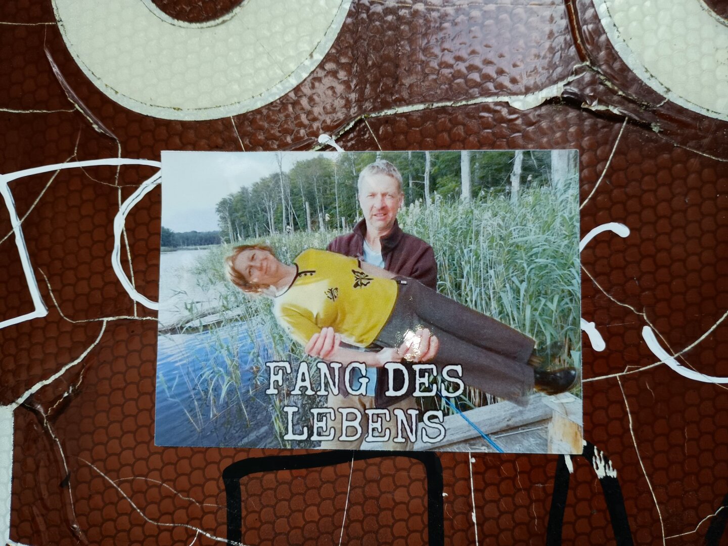 Foto eins Aufklebers mit der Aufschrit "Fang des Lebens". Dabei hält ein Mann seine Frau auf dem Arm.