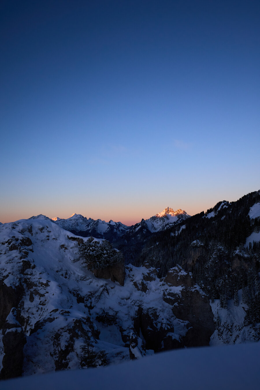 A small peak over some snow on a mountain top light up by the dawn.