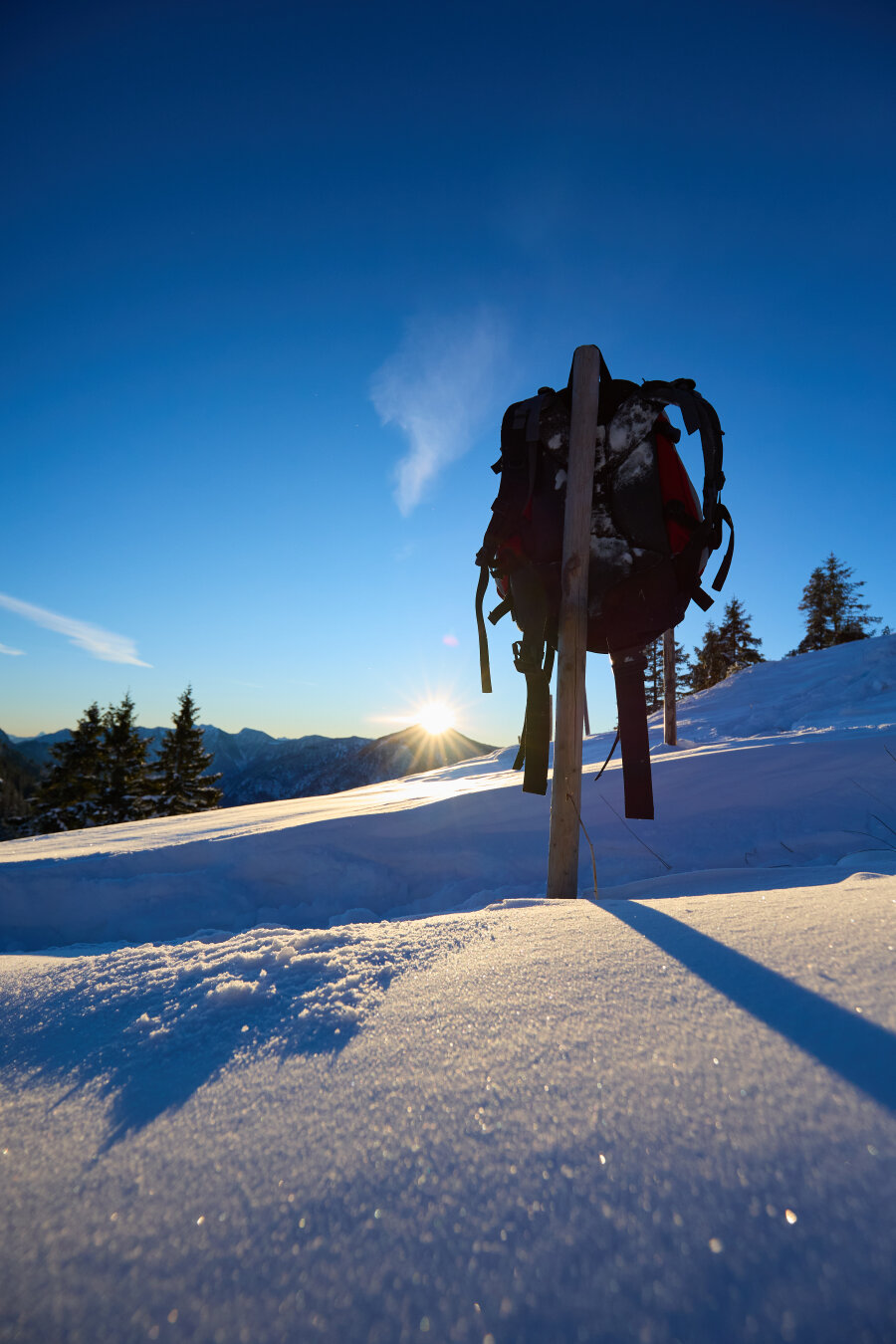 The sunrise with a backpack on a fence pole in the foreground and a snowy ground.