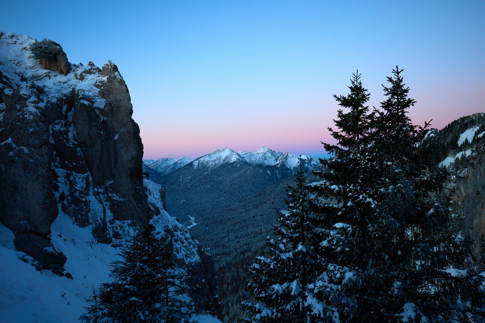 The view of a mountain with a beautiful red/orange/pink dawn behind it thorugh a rock and some trees in the foreground.