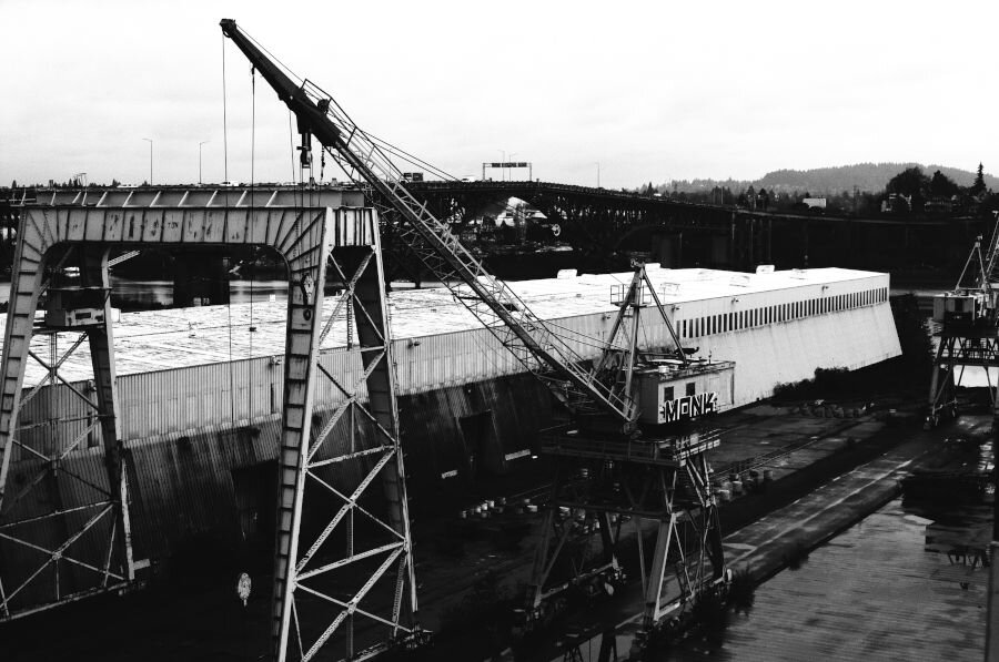 A large gantry crane and a smaller but still massive boom crane on wheels. They are rusty and have some graffiti on them.