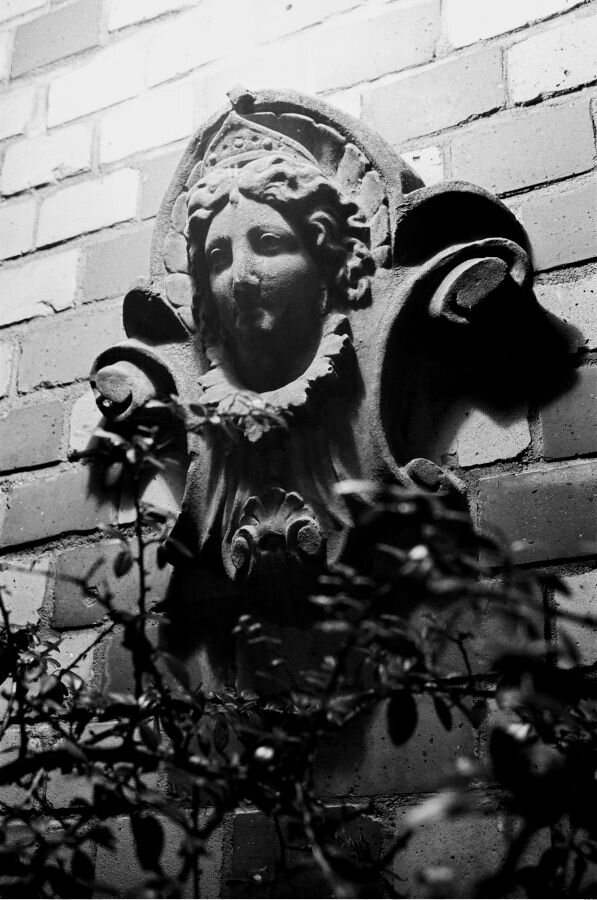 A decorative angel or goddess face on the side of a brick building, lit by a porch light.