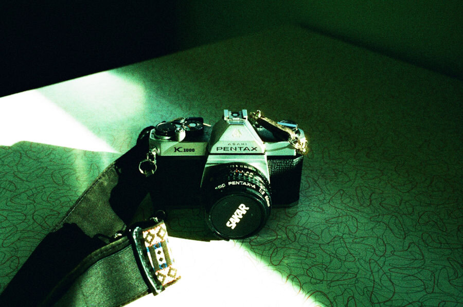 A vintage Pentax camera sitting on a diner table. Everything has a cyan cast.