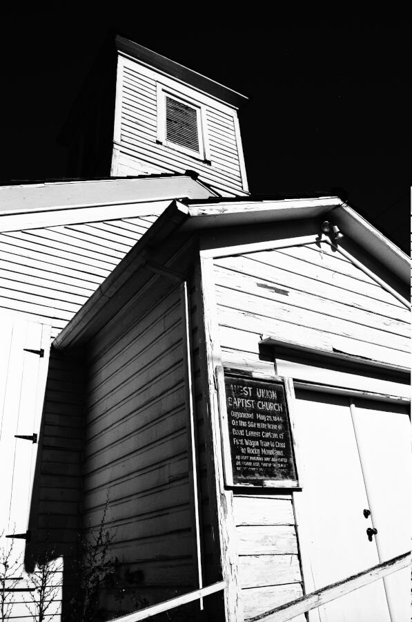 An old white wooden church against a black sky. The paint is peeling.