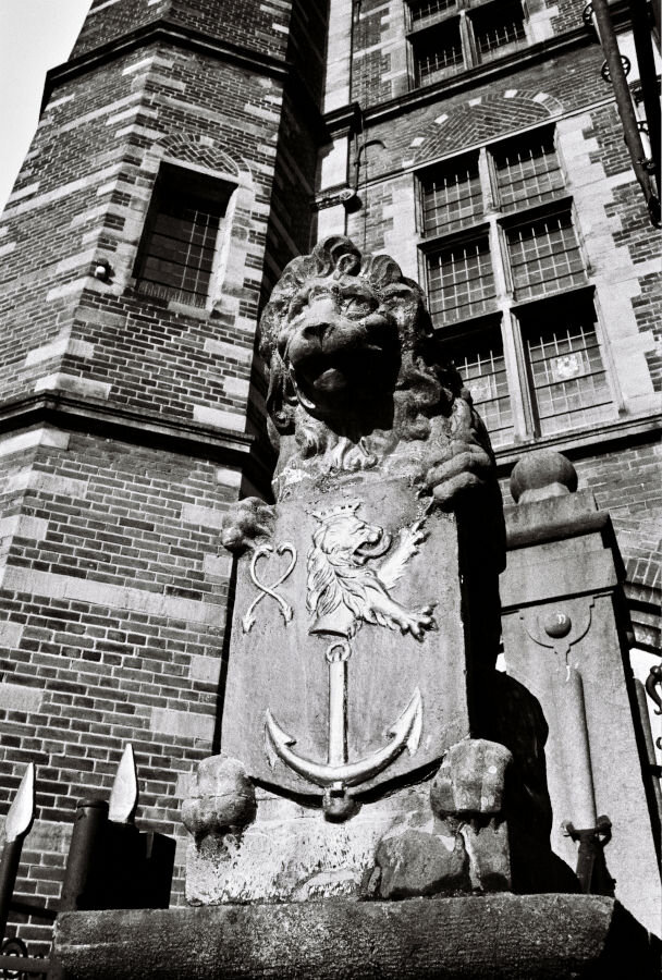 A stone lion in front of a Renaissance-era brick building. The liion holds a crest with a lion and an anchor.