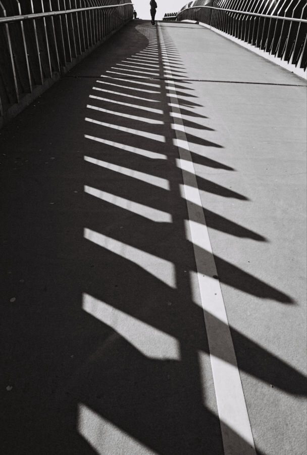 Shadows of the railng on a pedestran bridge with two lanes, one for bikes, one for people.