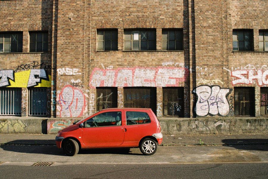 A small red car parked in front of a graffitied brick wall