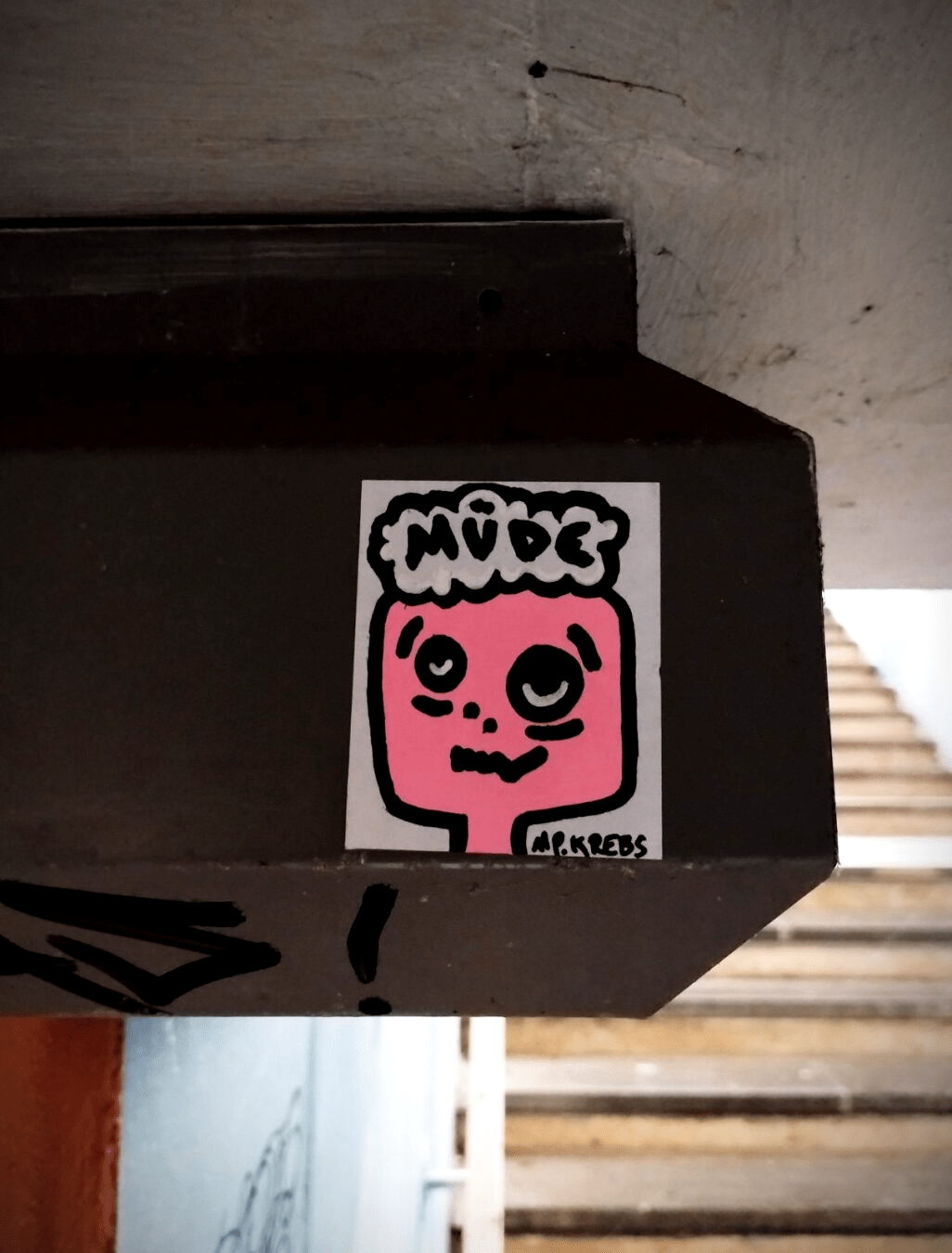 Aufkleber mit müden Gesicht und "Müde" Gedankenblase neben Treppenaufgang am Bahnhof.