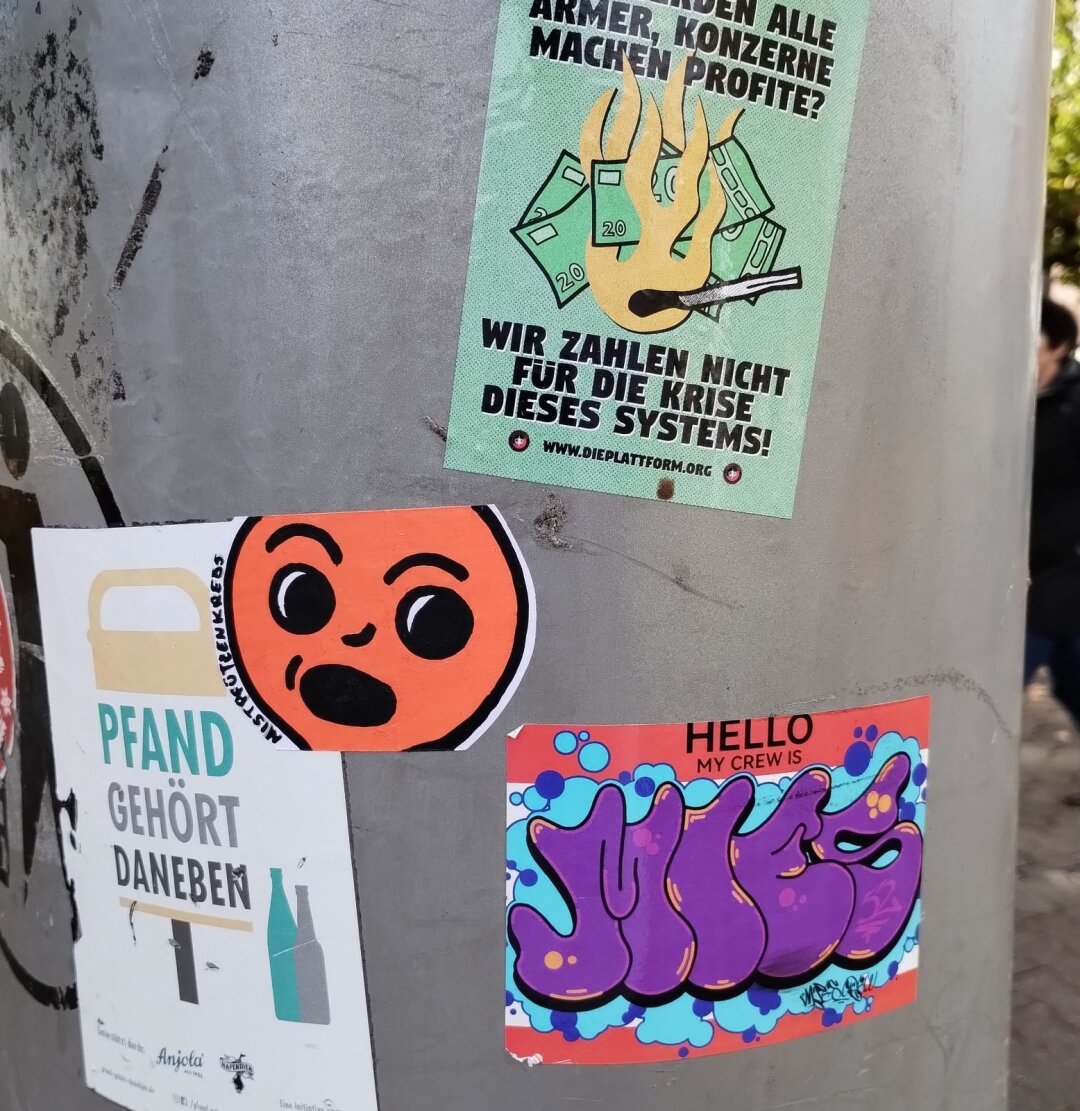 Aufkleber auf Mülleimer. Ein Gesicht schaut erstaunt ein Graffiti an.