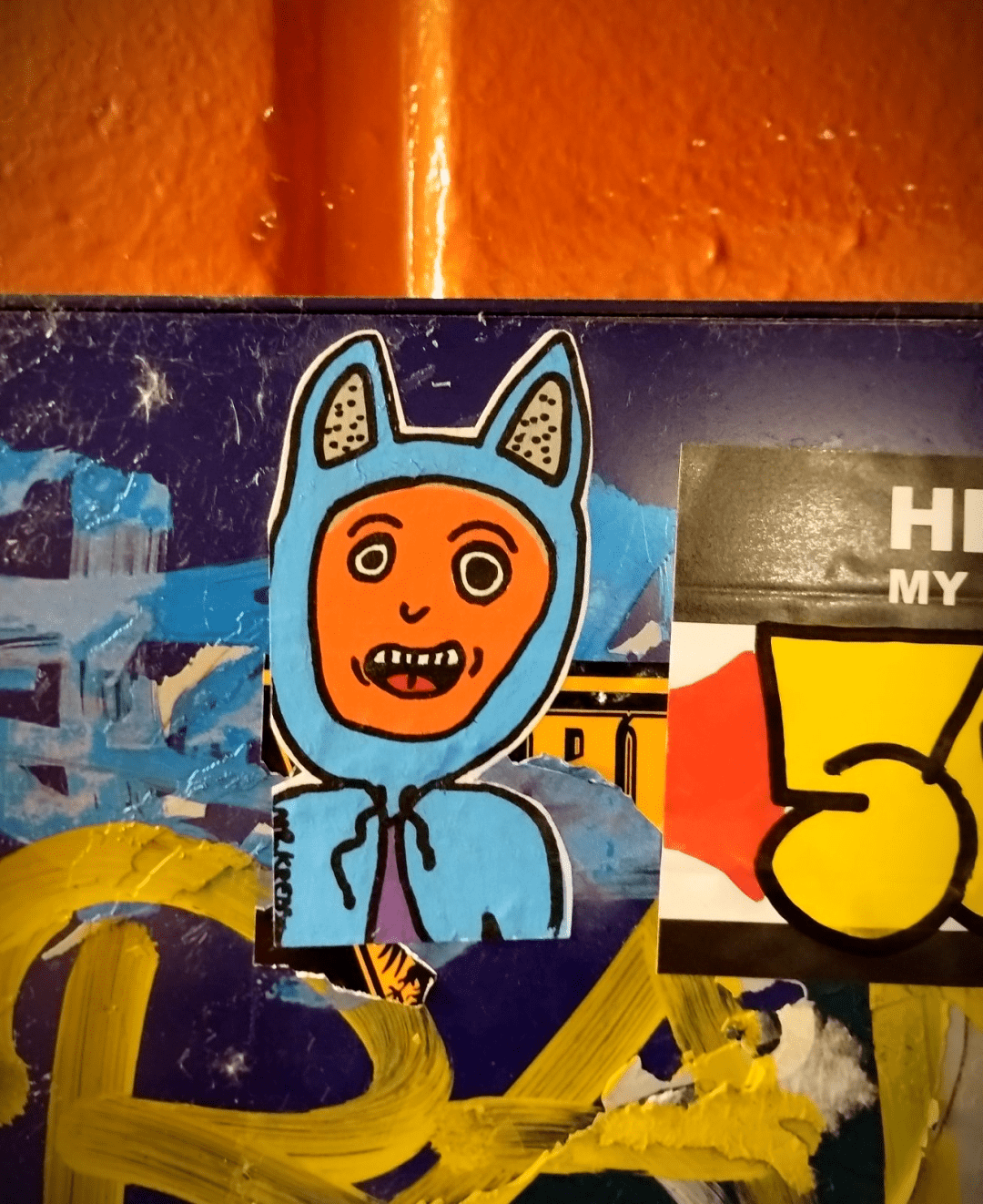 Aufkleber einer lachenden Figur welche einem Kaputzenpulli mit Katzenohren an hat.