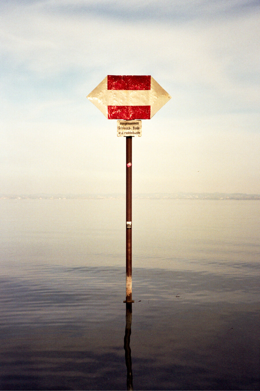 Traffic sign with two red arrows pointing in opposite directions on a pole in Lake Constance at Bregenz. Small sign with text below the arrows. *** Verkehrsschild mit zwei roten Pfeilen, die in entgegengesetzte Richtungen zeigen, auf einem Pfahl im Bodensee bei Bregenz. Kleines Schild mit Text unter den Pfeilen.