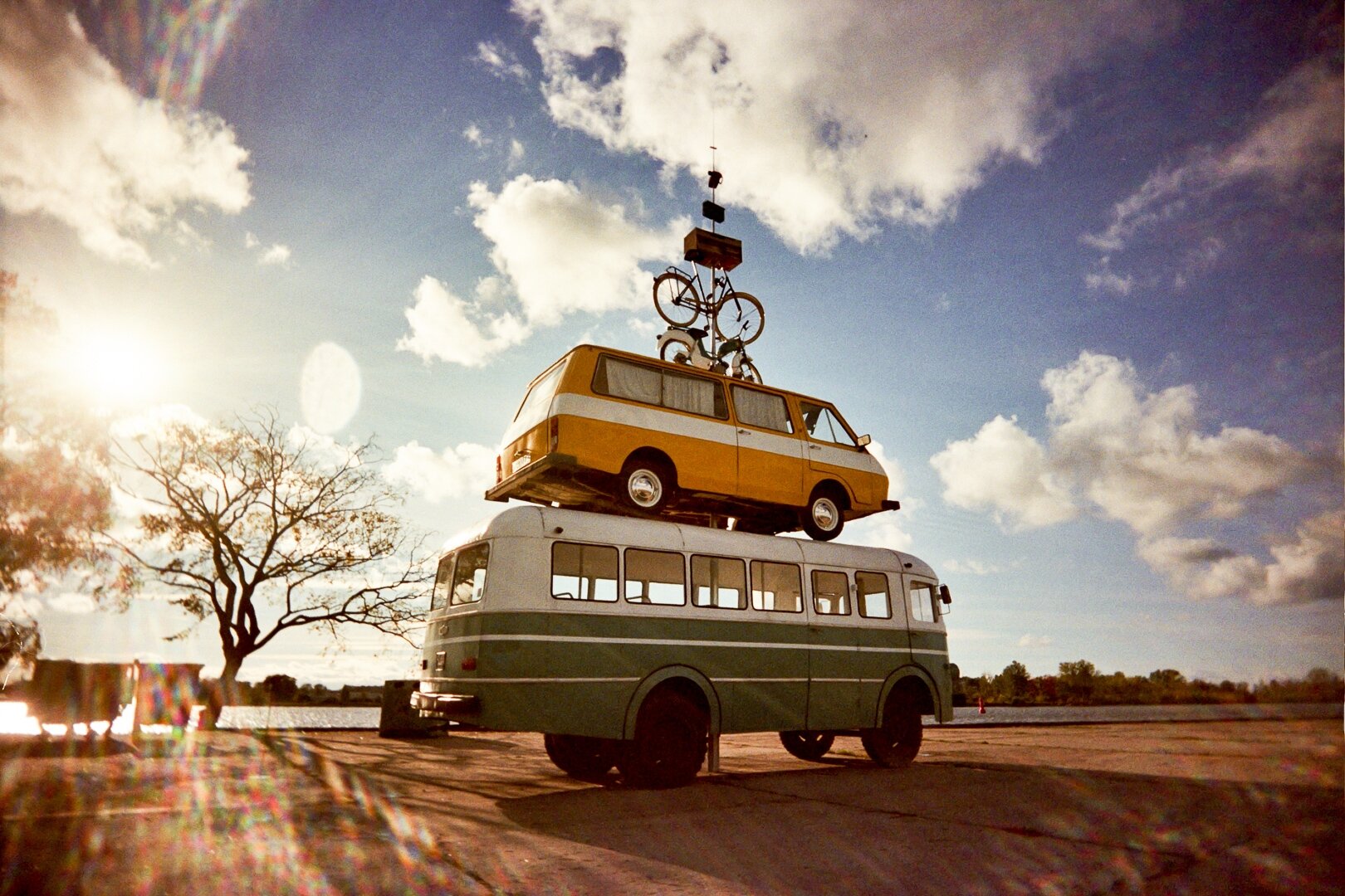 A green bus with a yellow-and-white minibus on its roof, topped by a bicycle, under a cloudy sky in Riga. *** Ein grüner Bus mit einem gelb-weißen Kleinbus auf dem Dach, auf dem ein Fahrrad montiert ist, vor bewölktem Himmel in Riga.