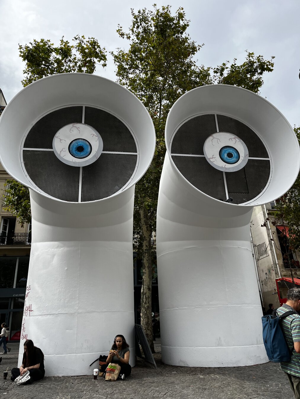 Deux yeux regardent des gens assis face au Centre Pompidou à Paris