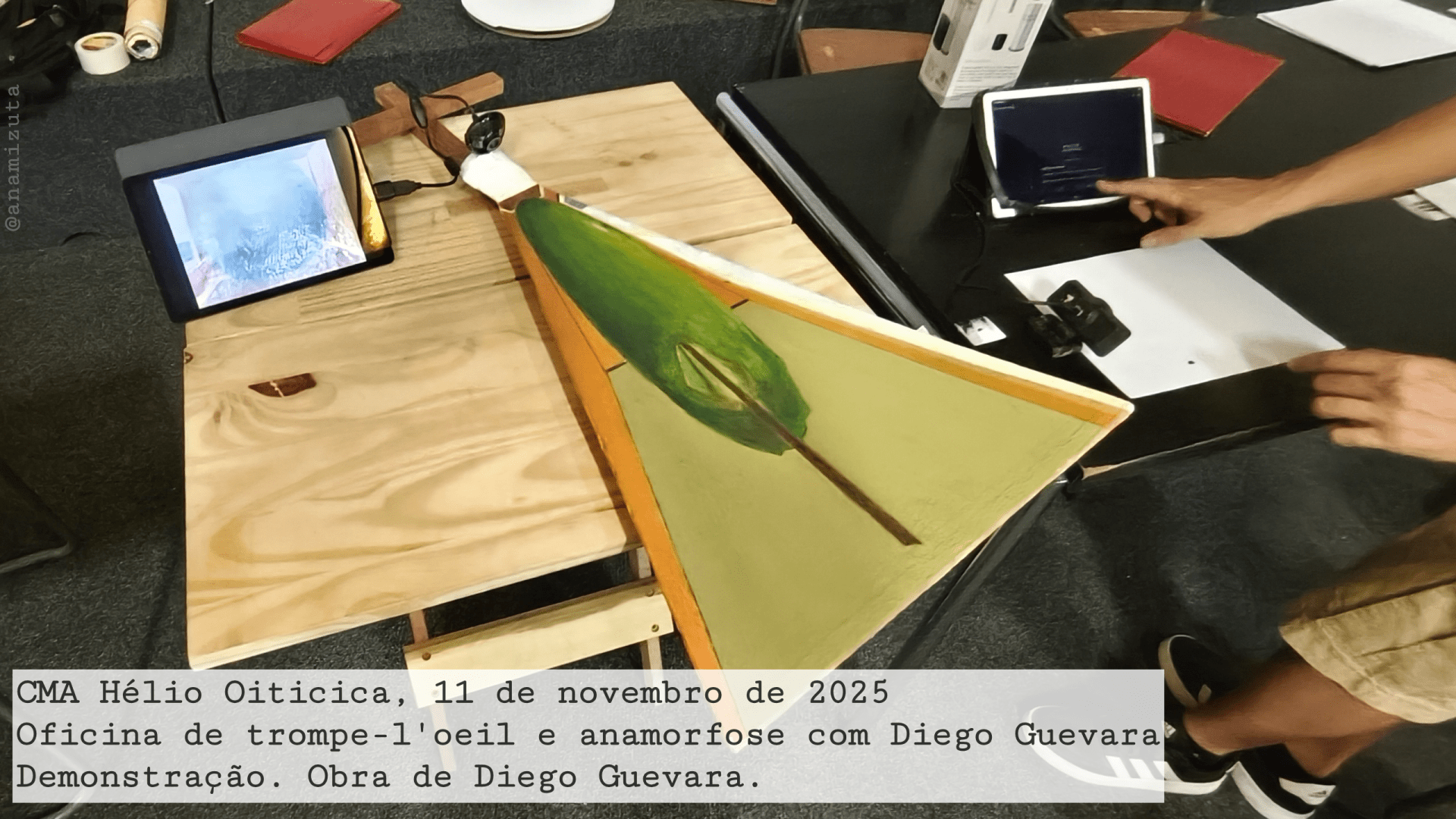 Artwork by Diego Guevara. A camera points at a distorted Magritte painting, "The Listening Room", a giant apple in a room. The painting is at a 90 degree angle in front of the camera. The image appears undistorted on a tablet.