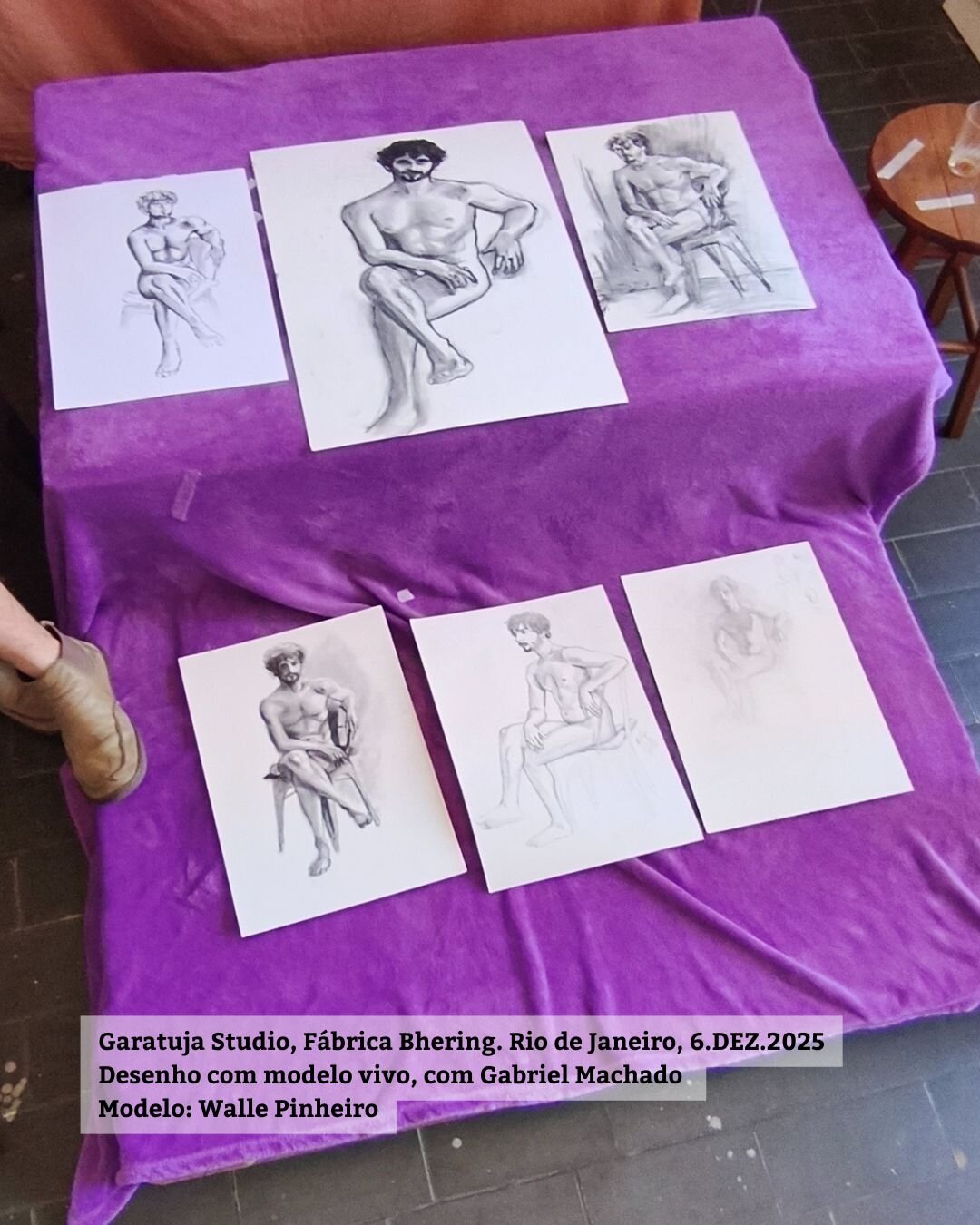 Foto mostra os vários desenhos dos participantes resultantes da sessão de modelo vivo. Os desenhos em papel branco estão cima de um pequeno tablado. Há desenhos a carvão e lápis. O modelo é um homem branco jovem e aparece sentado sobre uma cadeira em cima do tablado na pose final longa.