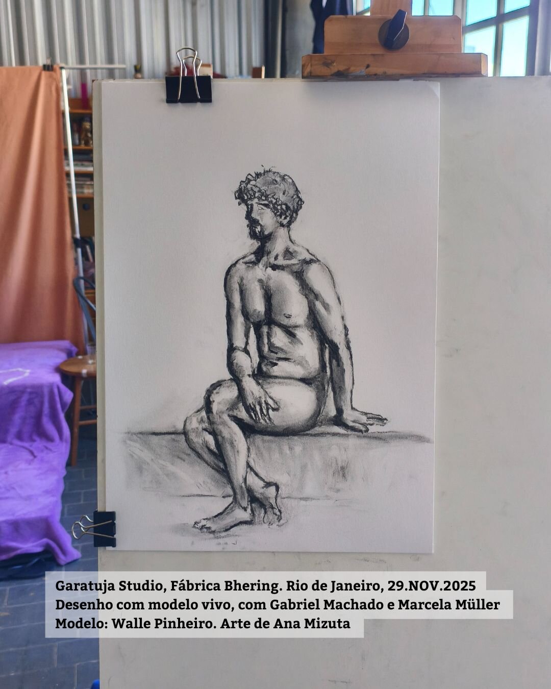 Foto do desenho final, de pose longa, que fiz. Ele está no cavalete e é um desenho a carvão sobre papel branco A3. O modelo, um homem branco, aparece sentado sobre o tablado.