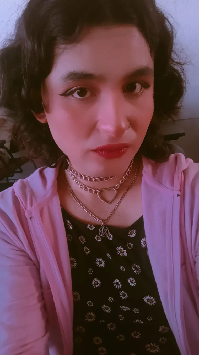 A selfie wearing the same flowery dress but now with a pink jacket.