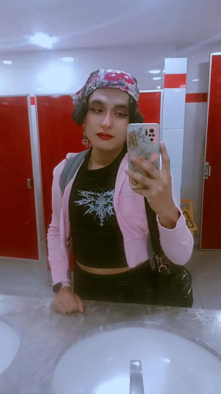 A mirror selfie wearing a witchy black T-shirt, a pink jacket and a colorful flowery headscarf.