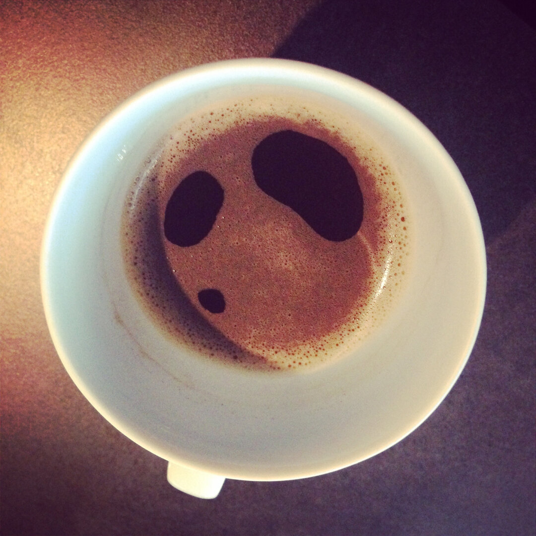 Eine Kaffeetasse zeigt auf ihrer Oberfläche Schaumflecken, die an ein Gesicht erinnern.