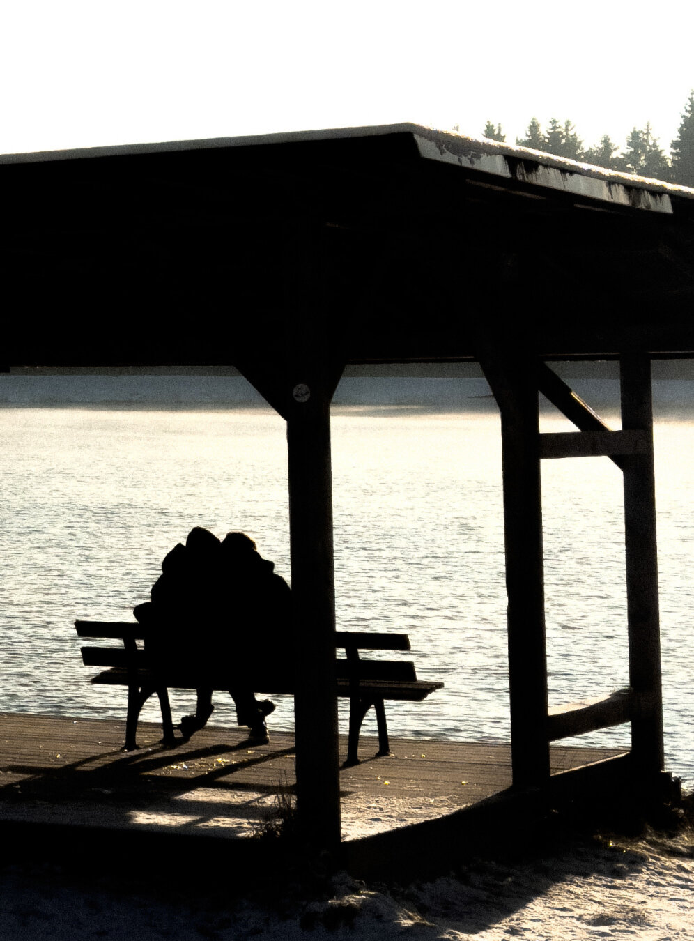 Ein Paar sitzt auf einer Bank unter einem Pavillon am Seeufer.